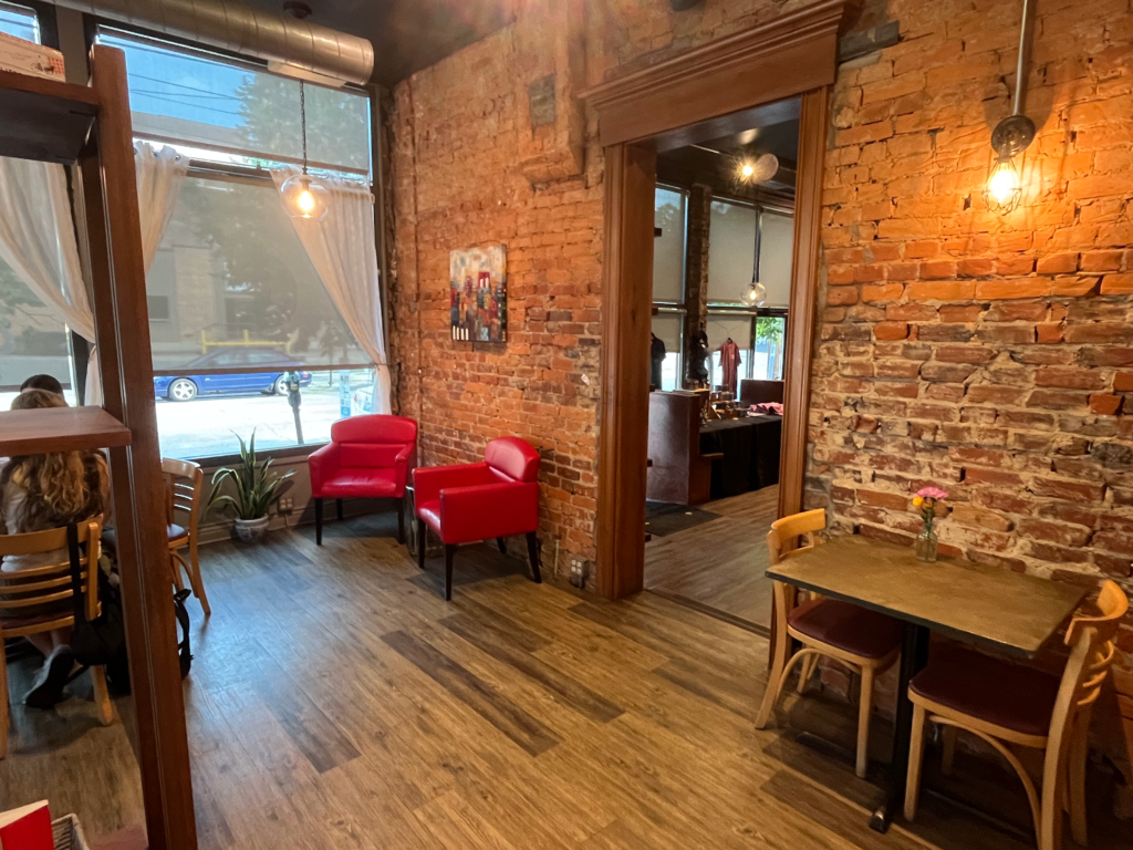 Two red leather cushioned chairs and a table beside a brick wall inside Carabello Coffee Company