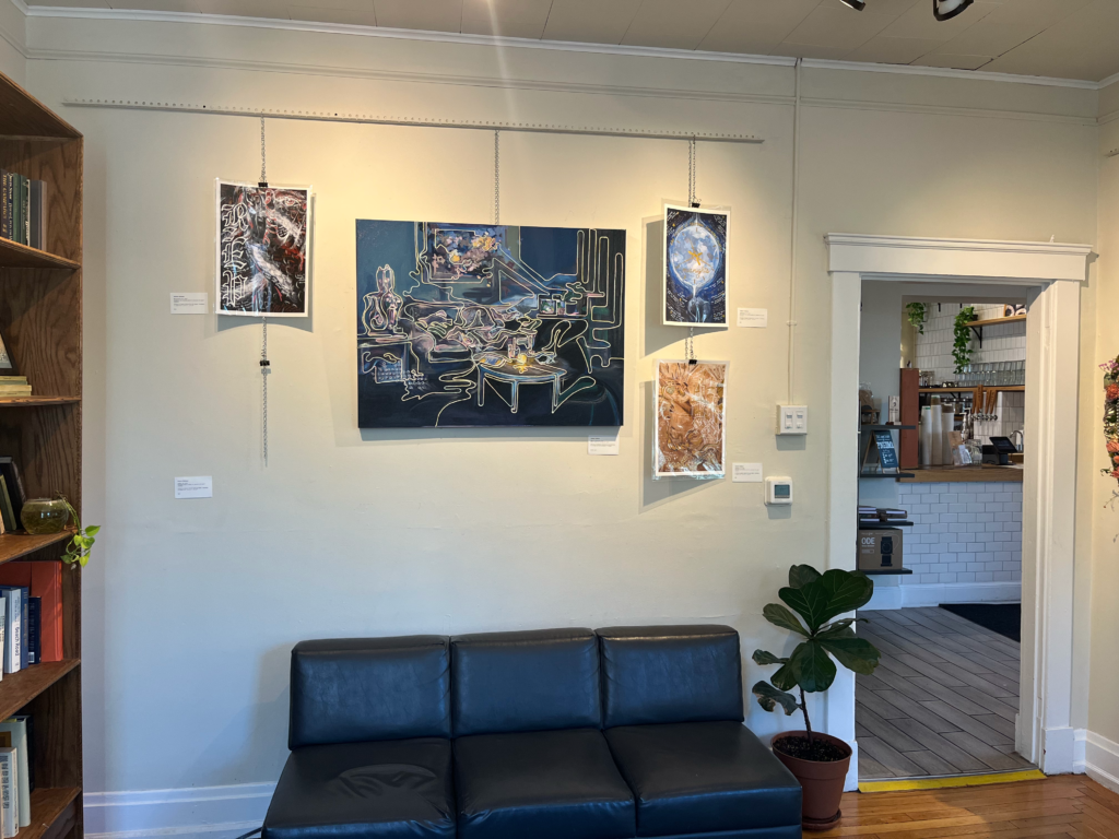 Art pieces hang over a couch and house plant in the art gallery inside Rohs Street Cafe