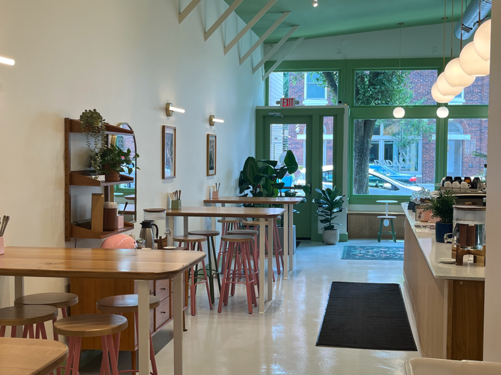 Wooden high tables in front of the green-trimmed front entrance of Urbana Cafe in Price Hill