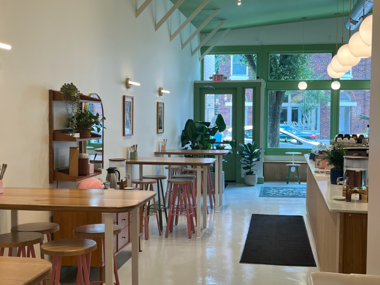 Wooden high tables in front of the green-trimmed front entrance of Urbana Cafe in Price Hill