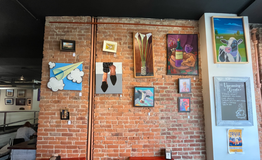 Framed pieces of art hanging on a brick wall in the art gallery inside The Upside Brew