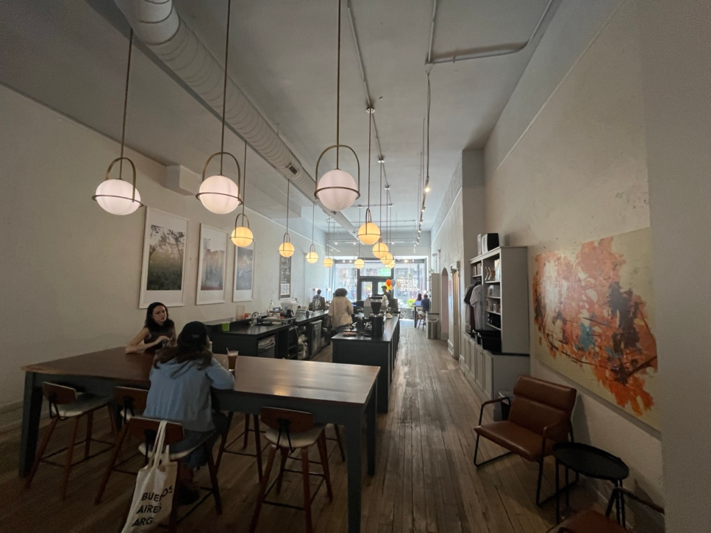 A large wooden table beneath spherical hanging light fixtures inside Deeper Roots Coffee on 4th Street