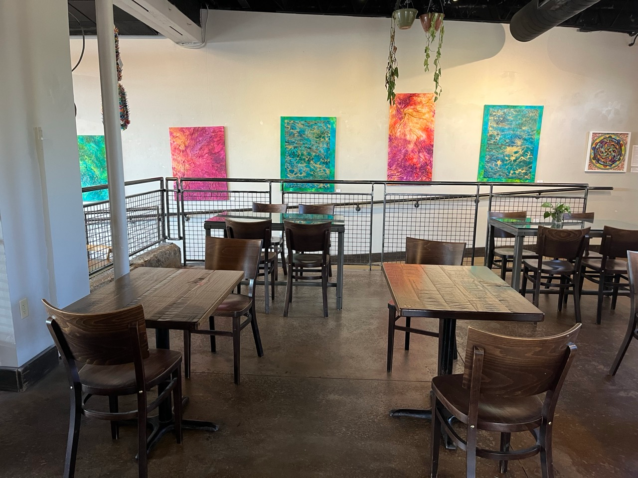 Five large paintings hang on the wall above wooden tables and chairs in Red Tree Coffee and Art in Oakley